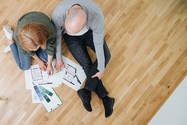 Pärchen von oben über Wohnungsplänen sinnierend